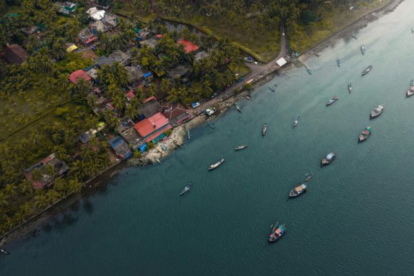 Aerial coastal view featuring boats and a village in GA, India.